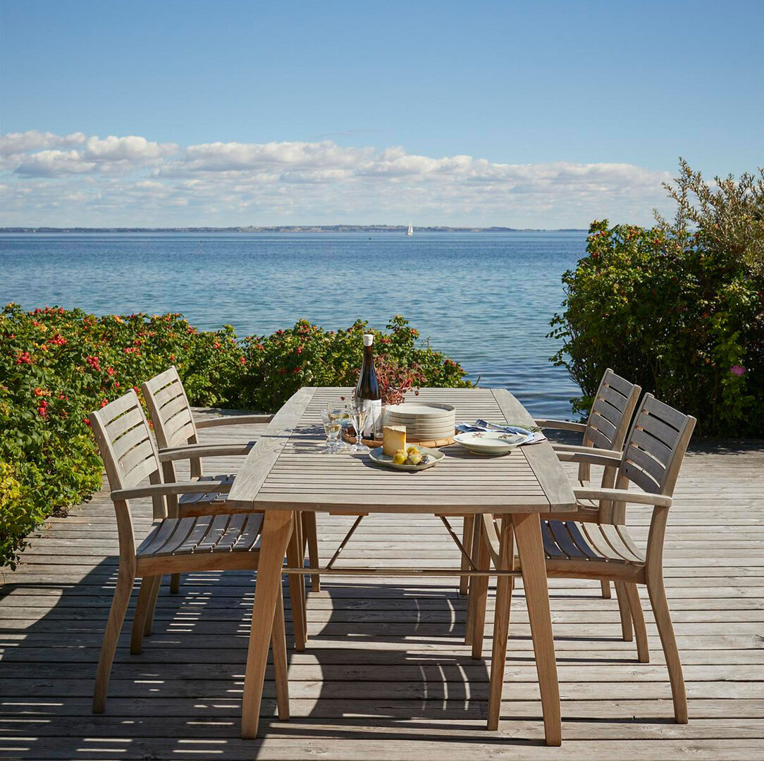 Skagerak Ballare Gartentisch und Stühle aus massivem Teakholz auf einer Holzterrasse am Wasser
